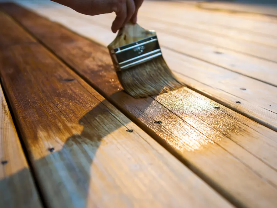Professional applying wood stain to a deck with a paintbrush